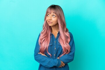 Young mixed race woman with pink hair isolated on blue background thinking an idea while looking up