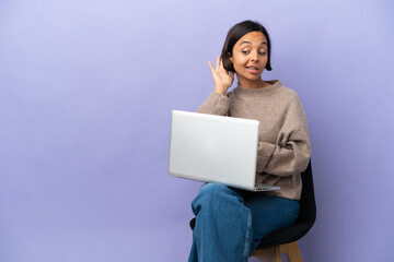 Young mixed race woman sitting on a chair with laptop isolated on purple background listening to something by putting hand on the ear