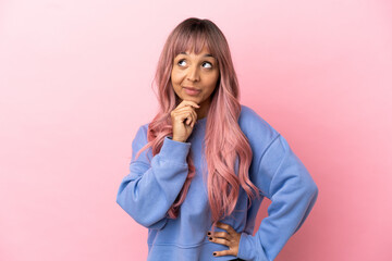 Young mixed race woman with pink hair isolated on pink background thinking an idea while looking up