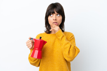 Young mixed race woman holding coffee pot isolated on white background having doubts and thinking