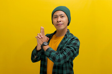 Young Asian man, dressed in a beanie hat and casual shirt, makes a finger gun gesture, mimicking...