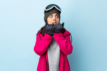 Mixed race skier girl with snowboarding glasses over isolated blue background nervous and scared putting hands to mouth.