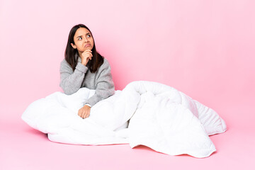 Young mixed race woman wearing pijama sitting on the floor having doubts and thinking