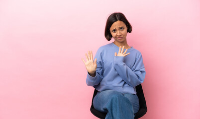 Young mixed race woman sitting on a chair isolated on pink background nervous stretching hands to...