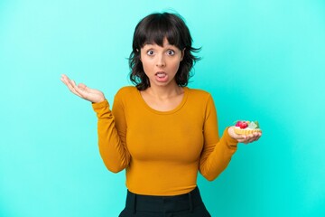 Young mixed race woman holding a tartlet isolated on blue background with shocked facial expression