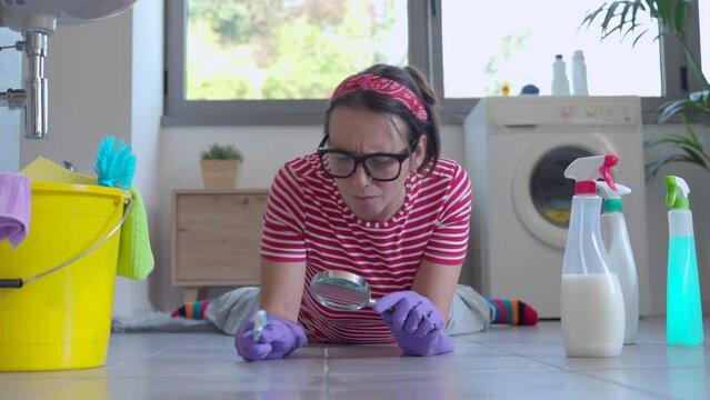 Woman cleaning the bathroom floor with a toothbrush and smiling, she is obsessed with hygiene
