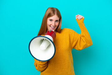 Young redhead woman isolated on blue background shouting through a megaphone to announce something