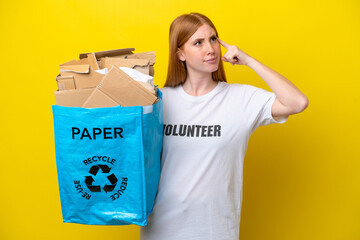 Young redhead woman holding a recycling bag full of paper to recycle isolated on yellow background...