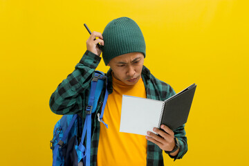 A confused young Asian student, dressed in a beanie hat and casual shirt with a backpack, scratches...