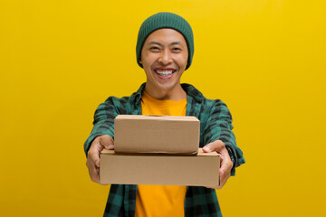A smiling Asian man, dressed in a beanie hat and casual shirt, holds a stack of package parcel...