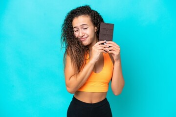 Young Arab woman isolated on blue background taking a chocolate tablet and happy