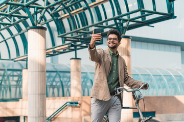 Young smiling man having a video call while pushing his bike in the city outdoors.