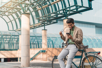 Smiling male business person texting on his mobile phone while sitting on a bike in front of an...