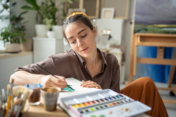 Calm female painter drawing with watercolor. Inspired pensive dreamy woman working on painting with...