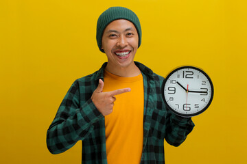 An excited young Asian man, dressed in a beanie hat and casual shirt, enthusiastically holds a...