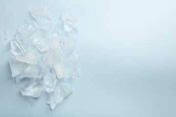 Pieces of crushed ice on light blue background, top view. Space for text