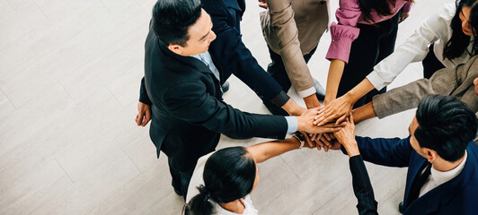 A top perspective reveals four diverse businesspeople standing in a circle stacking their hands....