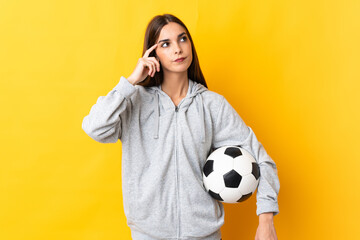 Young football player woman isolated on yellow background having doubts and thinking