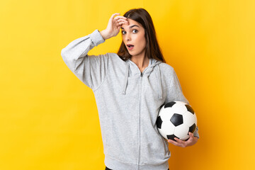 Young football player woman isolated on yellow background doing surprise gesture while looking to...