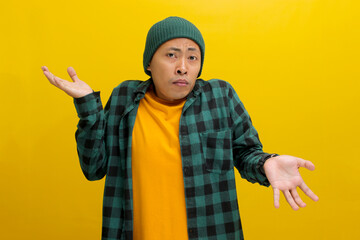 Confused young Asian man, dressed in a beanie hat and casual shirt is shrugging his shoulders in a...