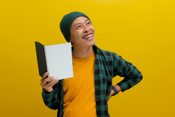An enthusiastic young Asian student, dressed in a beanie hat and casual shirt, holds a book while...