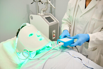 A person is getting a facial treatment with a green light led mask. Antiaging treatment.