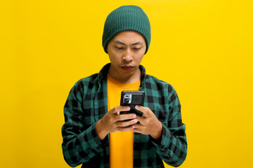 Happy and amazed Asian man, sporting a beanie hat and casual shirt, is using his smartphone for texting, social media engagement, online ecommerce shopping in mobile apps, or watching videos