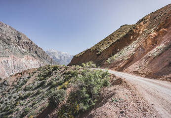 A dusty road winds in a mountain valley in the Fan Mountains in Tajikistan, a mountain road in the highlands