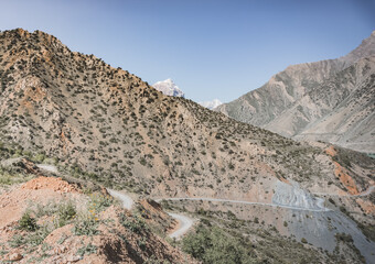 A dusty road winds in a mountain valley in the Fan Mountains in Tajikistan, a mountain road in the highlands