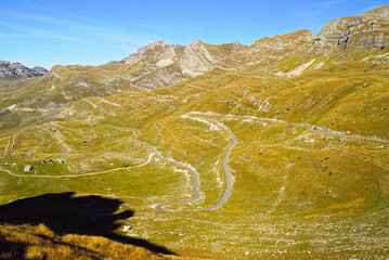 Top view of the Durmitor Ring panoramic road in Montenegro. A vibrant landscape with a mountain valley and a narrow, winding ribbon of dredge descending from the Sedlo pass in Durmitor National Park