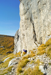 Hiking in Durmitor National Park, Montenegro: a tourist photographed from afar descends along a mountain path located near a picturesque cliff. Mount Sedlena Greda.