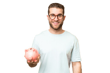 Young man holding a piggybank over isolated chroma key background smiling a lot