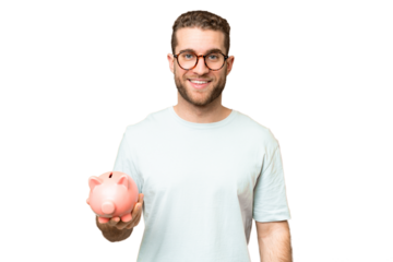 Young man holding a piggybank over isolated chroma key background smiling a lot