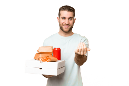 Young handsome blonde man holding pizzas and burgers over isolated background inviting to come with hand. Happy that you came