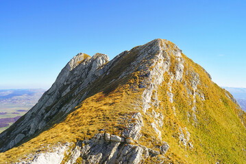 Southern peaks of Mount Sedlena Greda in Durmitor National Park (Montenegro). Bright autumn landscape from the highlands: slopes covered with yellow grass against the background of a blue sky