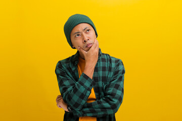 Thoughtful young Asian man, dressed in a beanie hat and casual shirt, appears concerned as he rests...