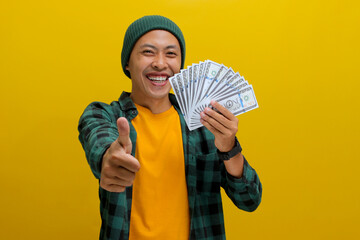 Enthusiastic Asian man in a beanie and casual clothes flashes a thumbs-up and waves a wad of cash....
