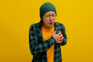 Young Asian man in a beanie hat and casual shirt is clutching his chest, displaying symptoms...
