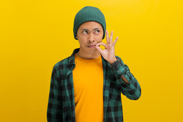A young Asian man, dressed in a beanie hat and casual shirt, is gesturing silence by sealing his...
