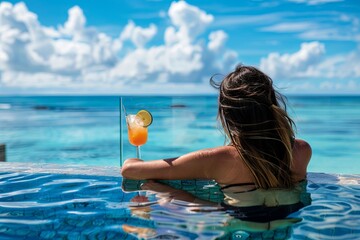 Brunette with cocktails relaxes in the pool, ocean in the background - obrazy, fototapety, plakaty
