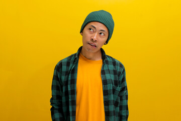 Hesitant young Asian man, dressed in a beanie hat and casual shirt, bites his lips, conveying a...