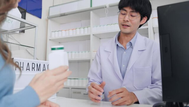 Asian customer female bring medicine bottle sample to apothecary man for consulting and buy back home in pharmacy.