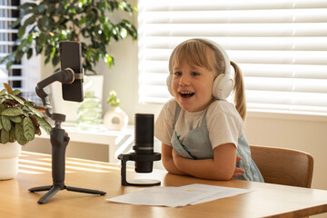 Young girl with headphones smiling during a solo podcast session, equipped with mic and smartphone. Podcasting.