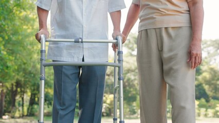 Asian senior woman support and help husband walking with walker cane in the garden, Physical therapy concept