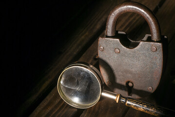 Old padlock and magnifying glass on the wooden desk table background. Secret information concept....