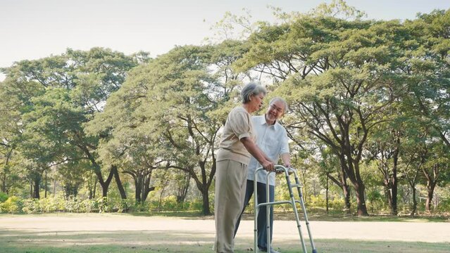 Asian senior man help and comfort wife walking with walker cane in the nature garden, Physical therapy concept