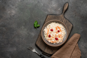 Sauerkraut with cranberries and carrots in a bowl on a wooden cutting board, dark grunge...