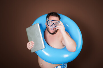 Funny fat man with an inflatable ring is going on vacation. Brown background.