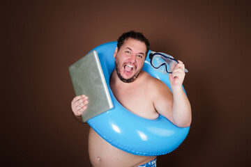 Funny fat man with an inflatable ring is going on vacation. Brown background.