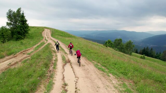 Three cyclists men riding electric bikes outdoors. Back view of male tourists biking in the mountains, wearing helmets and backpacks. Concept of sport, active leisure and nature.